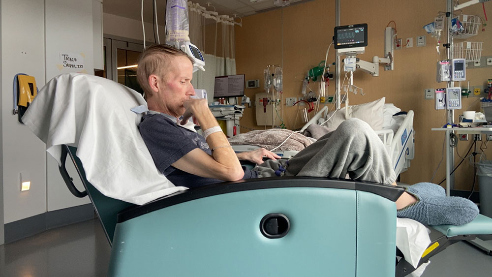 Seth Meyer sitting in chair and thinking in a hospital room.
