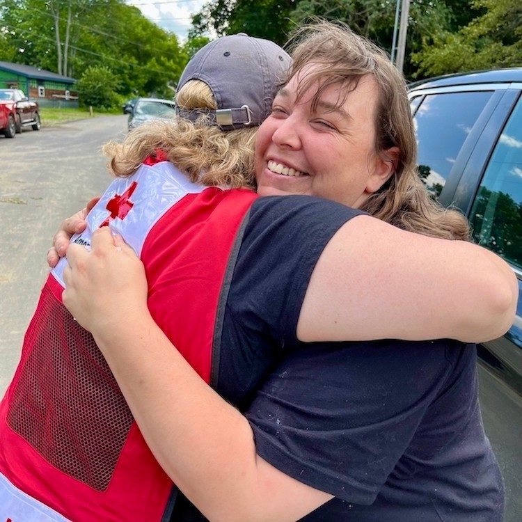 Volunteer in red vest hugging a client.