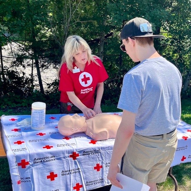 Red Cross volunteer explaining a CPR mannequin to a young man.