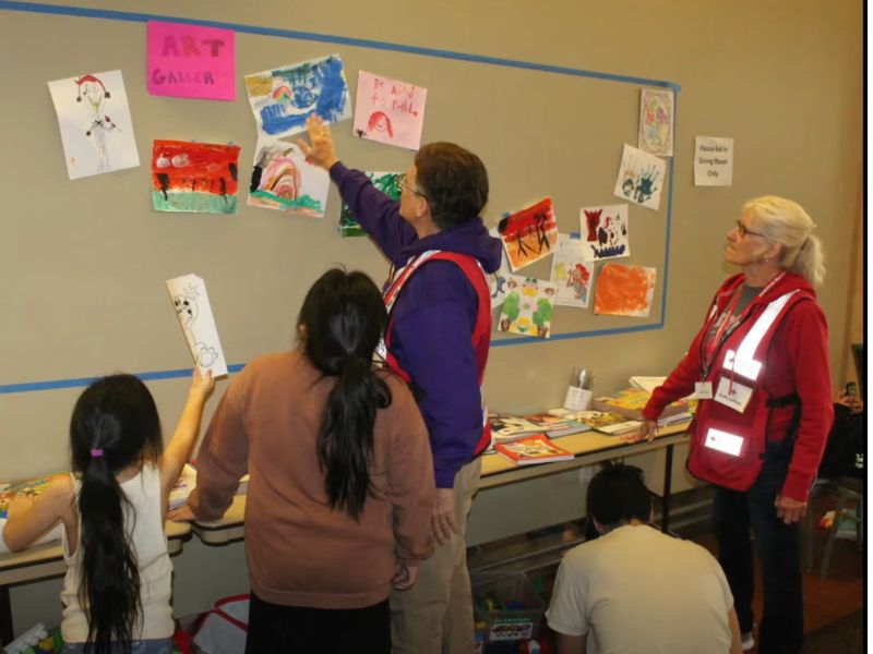 volunteers and children viewing drawings on art wall