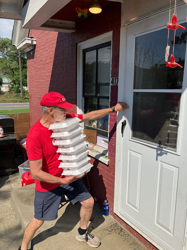Red Cross volunteer Pete Basiliere holding a stack of food containers and knocking on a house door.