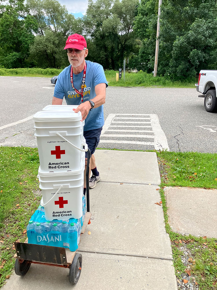 Red Cross volunteer Pete Basiliere pushing cart with bottled water and Red Cross 5 gallon buckets.