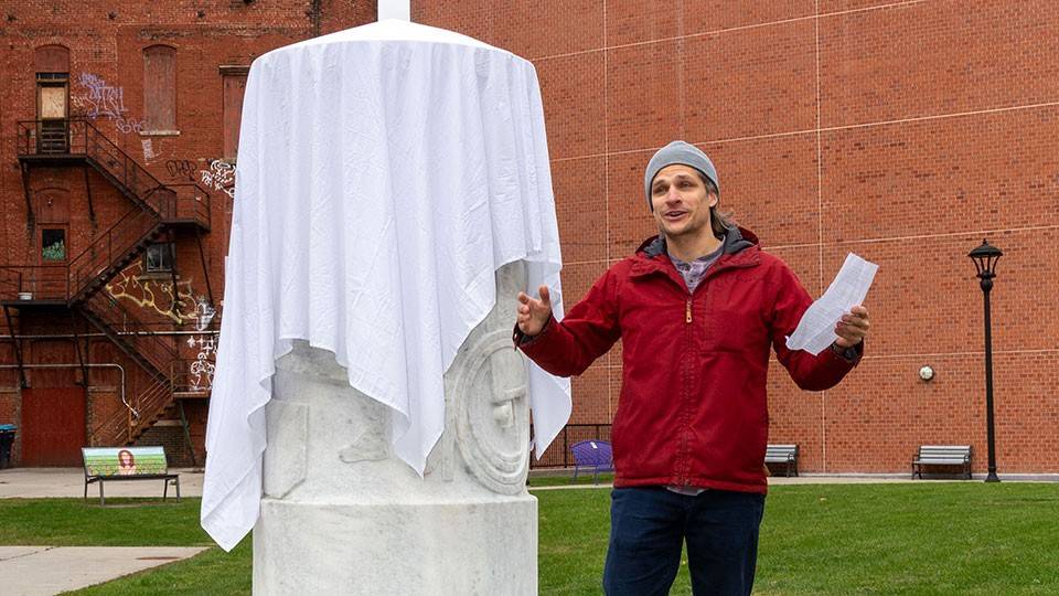 person standing next to a sculpture with a cloth covering it.
