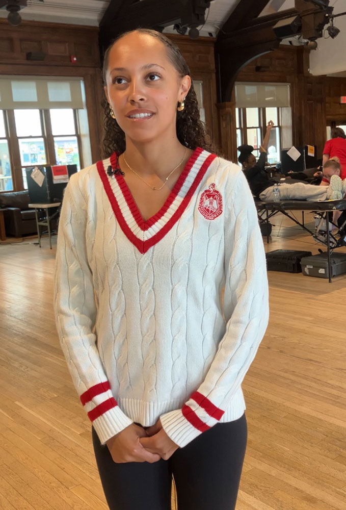 college student wearing a v-neck sweater at the blood drive inside a room where people are donating blood.