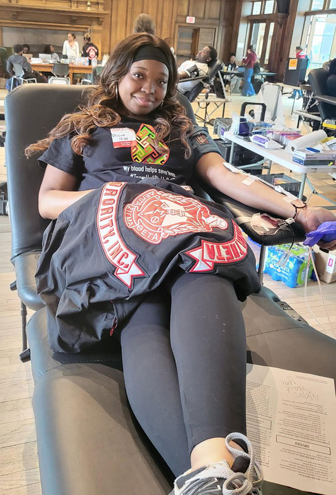 college student sitting in chair with jacket on lap, donating blood at the blood drive.