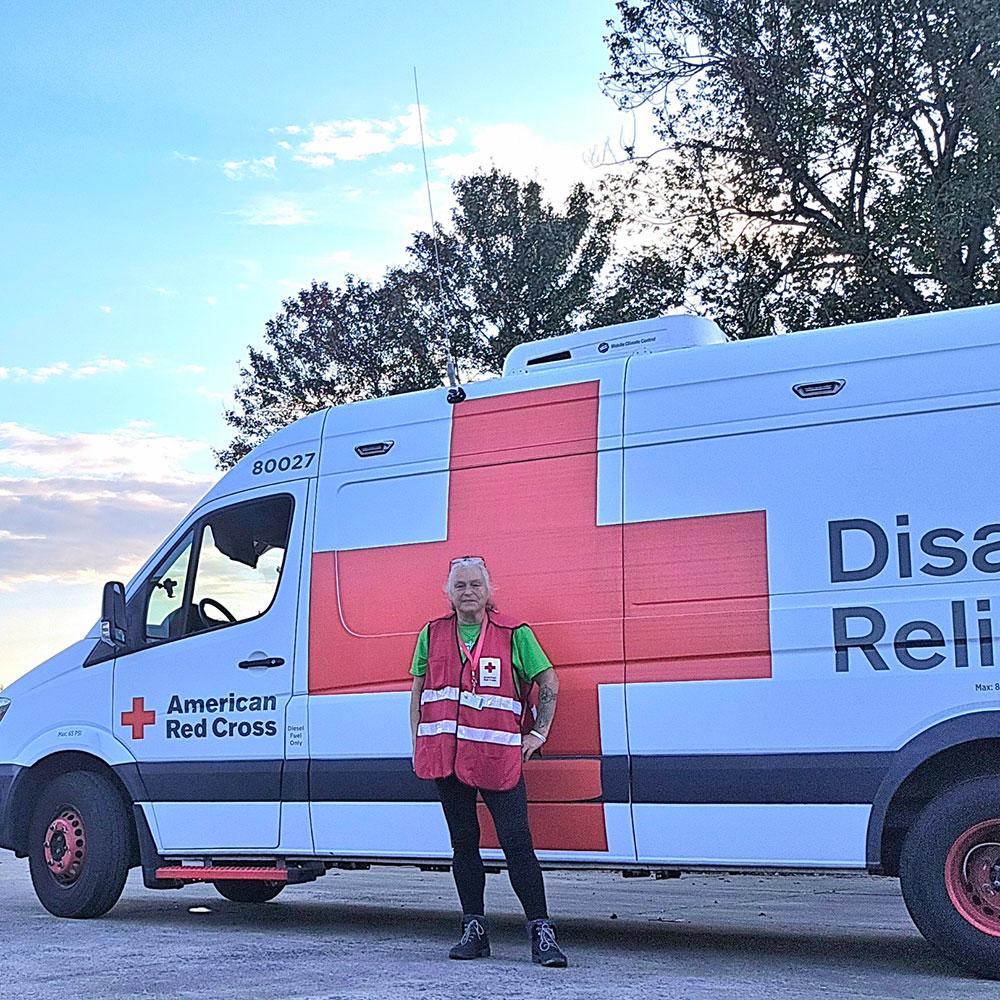 Red Cross volunteer Deb Wilson standing next to a Red Cross Disaster Relief vehicle.