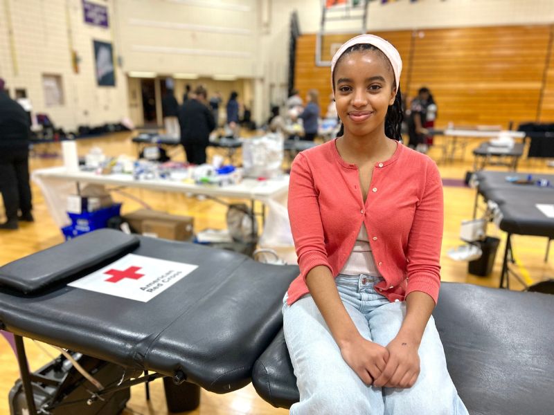 young woman sitting on red cross table about to donate blood