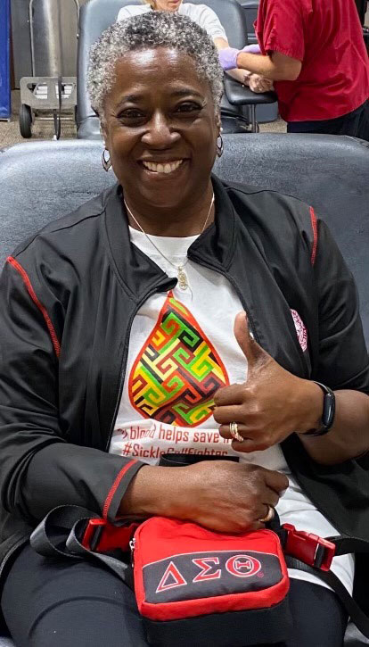 African American woman sitting in chair, smiling and giving a thumbs up while donating blood.