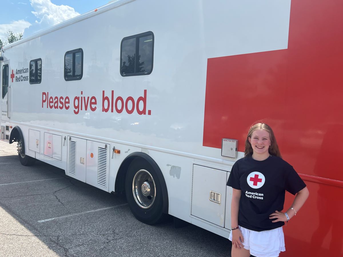 Maddie Frank standing next to a Red Cross blood donation bus in a red cross shirt