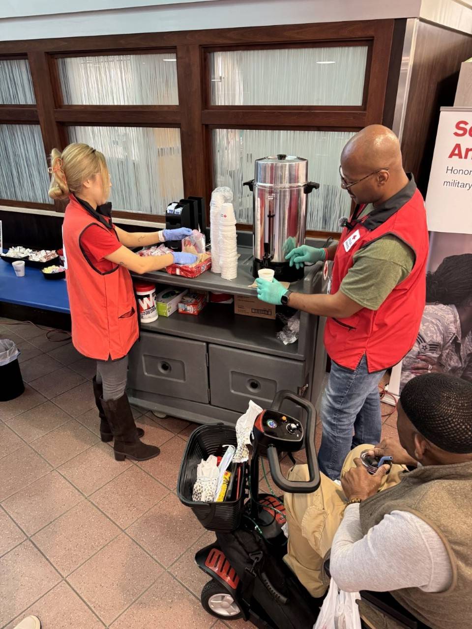 Two red cross volunteers serving coffee from a coffee cart
