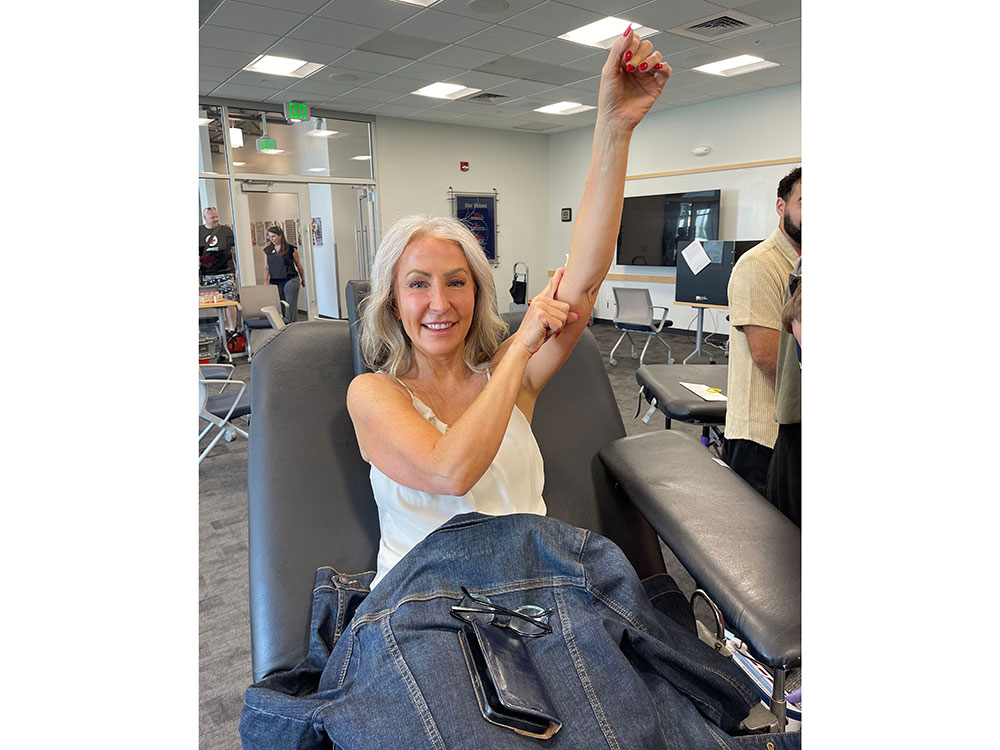 Person sitting in cot raising arm and holding gauze on arm and smiling for camera.