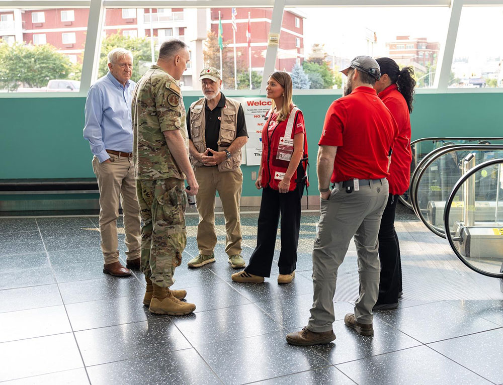 Red Cross staff members speaking to a military member in camouflage clothing.