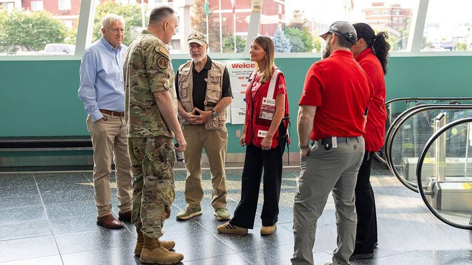 Red Cross staff members speaking to a military member in camouflage clothing.