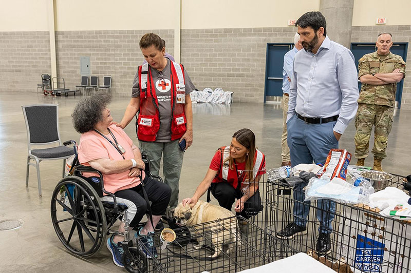 Red Cross staff members comforting a person in a wheelchair and her small dog.