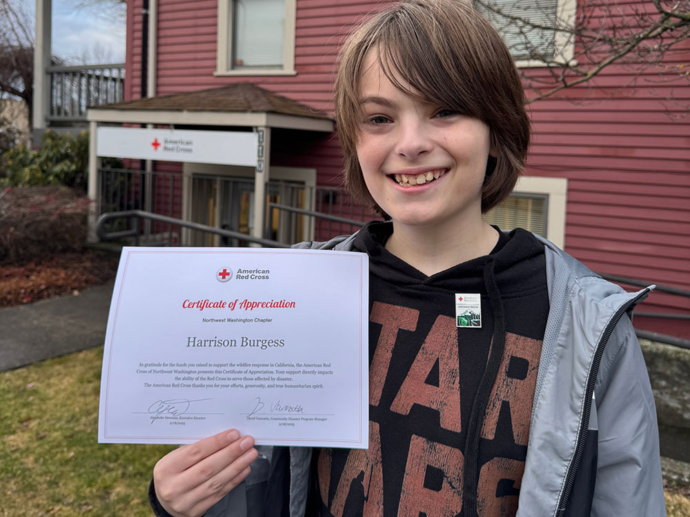 Harrison Burgess holding up an American Red Cross certificate of appreciation award in front of a Red Cross building.