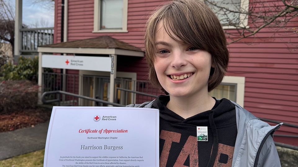 Harrison Burgess holding up an American Red Cross certificate of appreciation award in front of a Red Cross building.