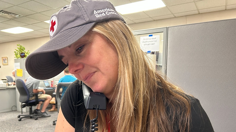 Red Cross volunteer Megan Snow wearing a Red Cross hat and answering phone calls in an office.