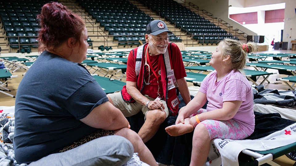 Dr. Thomas Barela, an American Red Cross disaster health services volunteer from Seattle, visits with Amber and her family at the Red Cross shelter in Perry, Florida, after Hurricane Helene devasted the family's home.