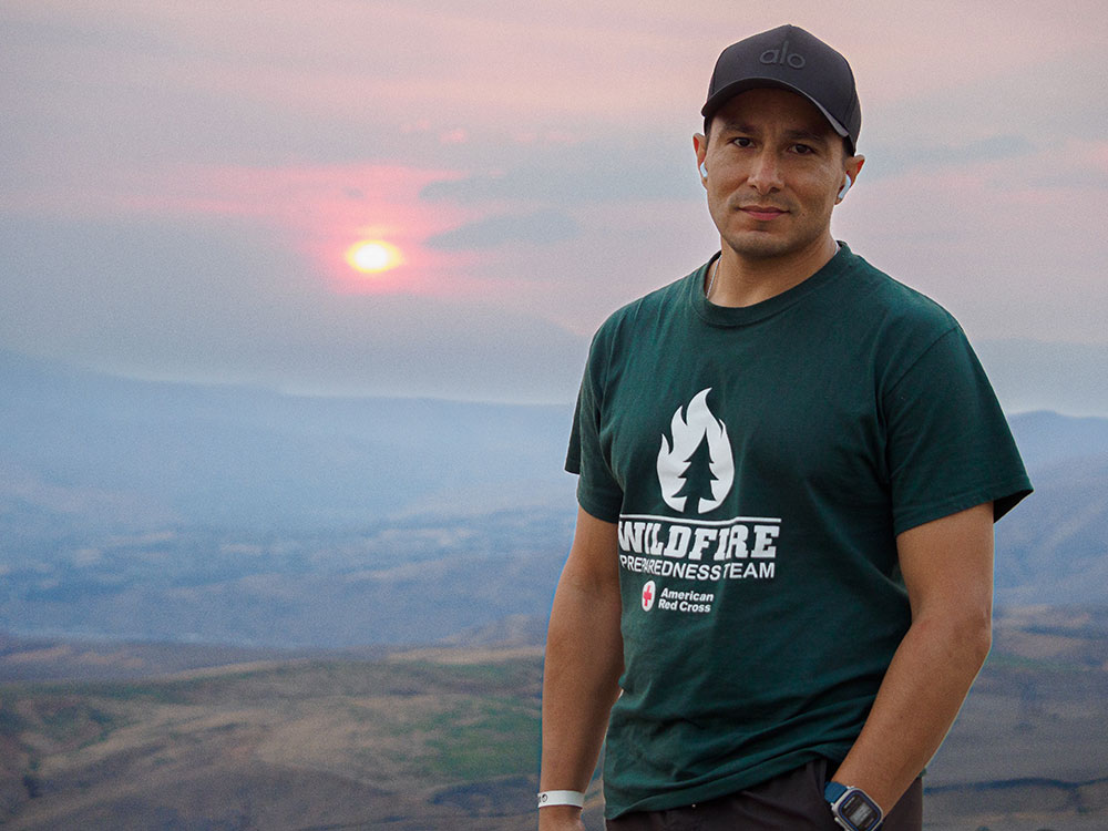 Wesley D. Clarillos wearing a hat and a Wildfire Red Cross shirt with the sunset in the background.