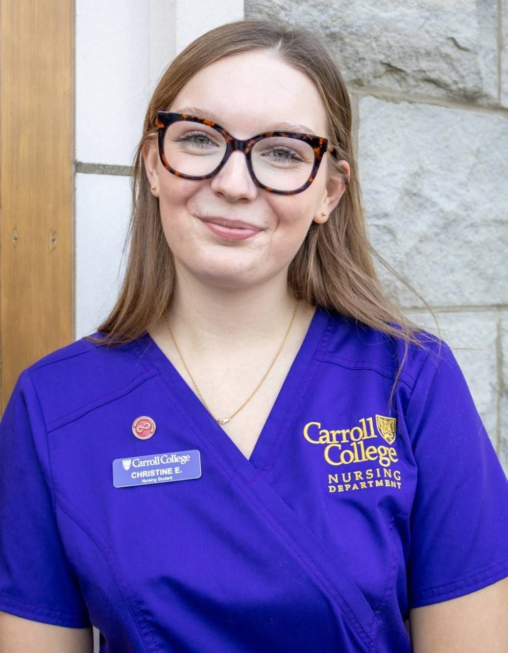 Woman wearing glasses and purple scrubs.