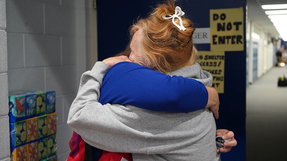 A Red Cross volunteer hugging another person in a shelter.