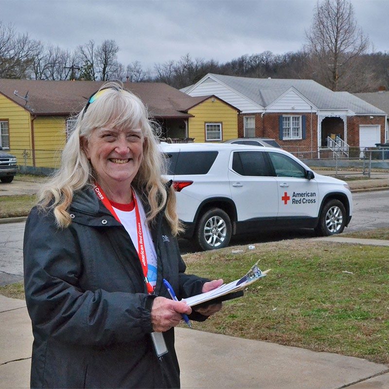 Red Cross volunteer holding clipboard and smiling.