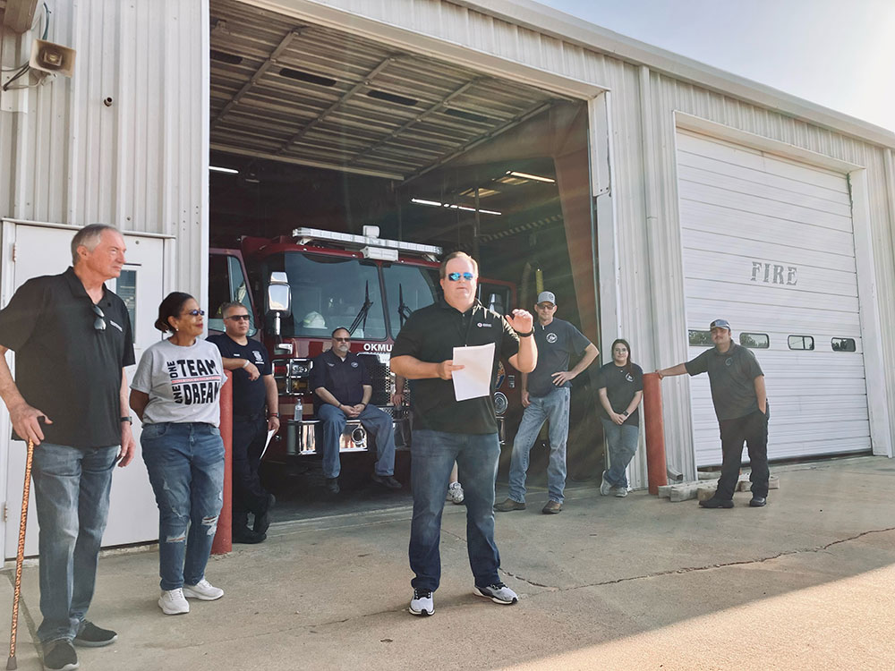 Hunter Harris talks to volunteers gathered at the Okmulgee Fire Station with fire engine in the background.