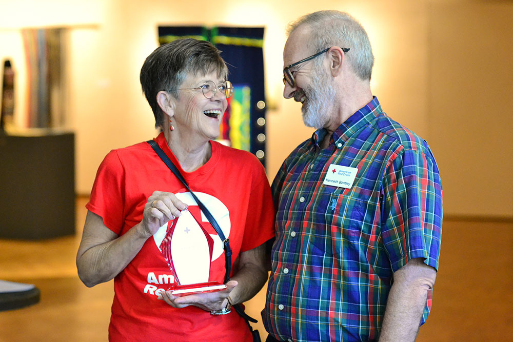 Patti Coley holding the 2026 Clara Barton Award for Meritorious Volunteer Leadership and standing next to Volunteer Services Senior Engagement Specialist Kenneth Bentley.