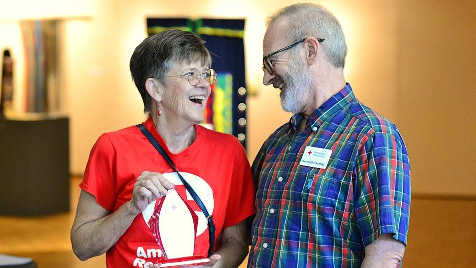 Patti Coley holding the 2026 Clara Barton Award for Meritorious Volunteer Leadership and standing next to Volunteer Services Senior Engagement Specialist Kenneth Bentley.
