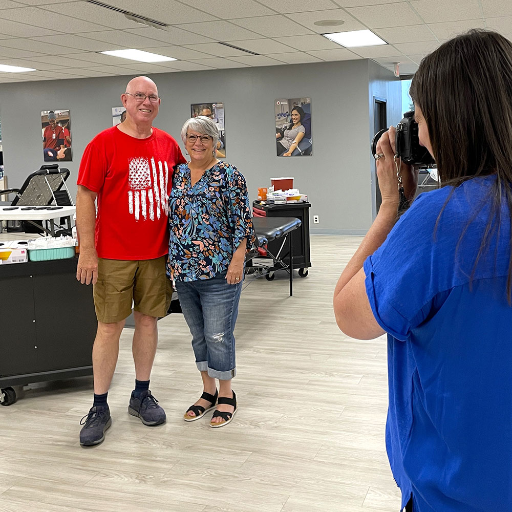 Al and Carol Cherry in a blood donation room, smiling for picture being taken by another person.