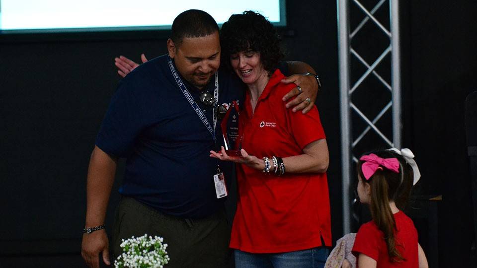 Kate Collins receiving the Clara Barton Award from Community Disaster Program Manager Karvin Vega while her daughter looks on.