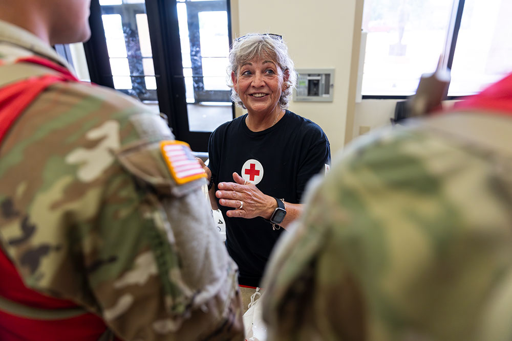 Red Cross volunteer speaking with military members in camo clothing.