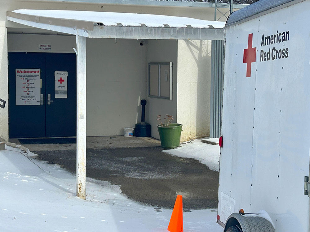 A red Cross trailer parked outside a shelter on a snowy day.