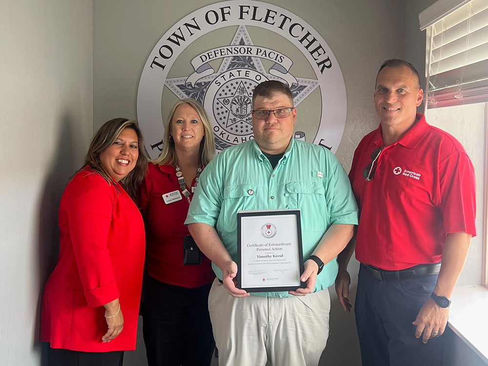 Timothy Kreul holding an American Red Cross Lifesaving Award while standing next to three Red Cross staff members.