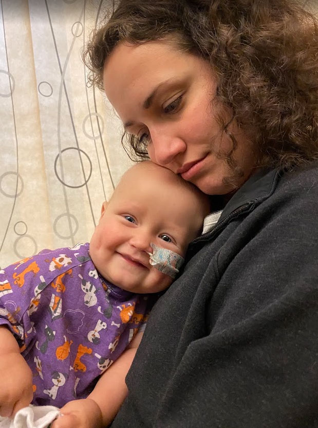 woman holding her baby that has a bandage holding a tube in his nose.