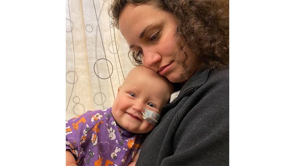 woman holding her baby that has a bandage holding a tube in his nose.