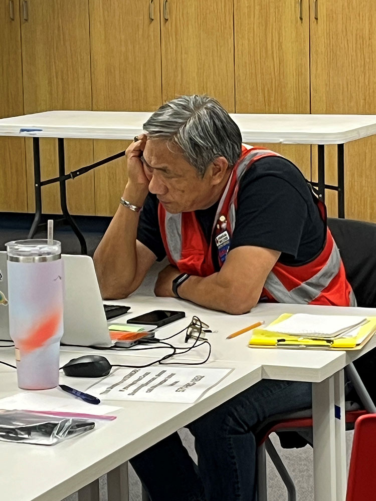 Dan Lam wearing a Red Cross vest and sitting at a desk working on a computer.