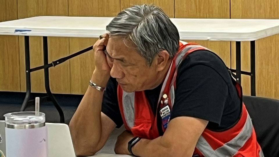 Dan Lam wearing a Red Cross vest and sitting at a desk working on a computer.
