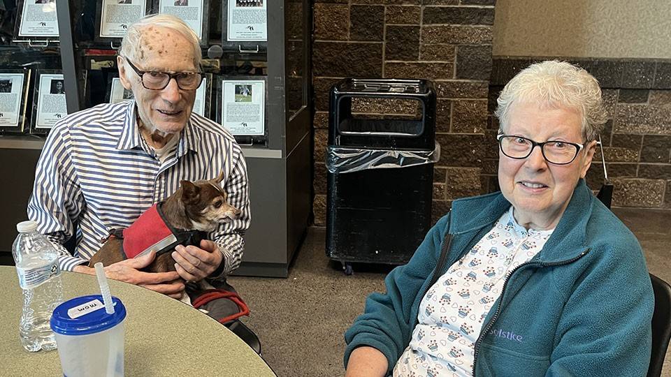 Darold and Marylee Dilley sitting at a table in a Red Cross shelter while holding their small dog.