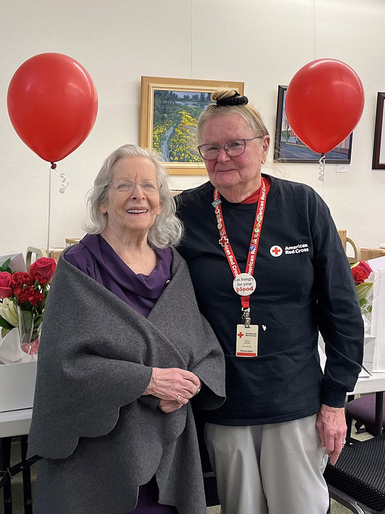 Elaine Yearsley and Ginny Greiner standing next to a table with flowers and balloons.