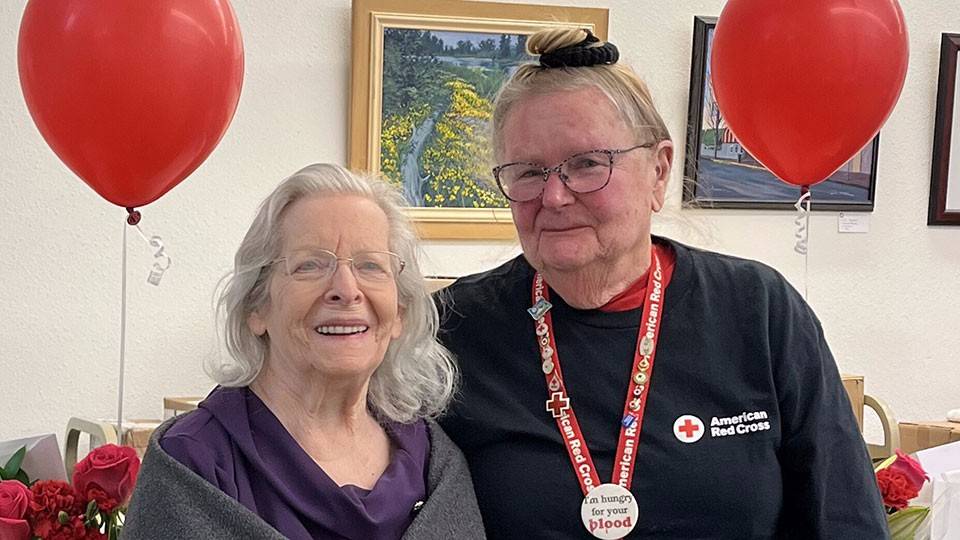 Elaine Yearsley and Ginny Greiner standing next to a table with flowers and balloons.