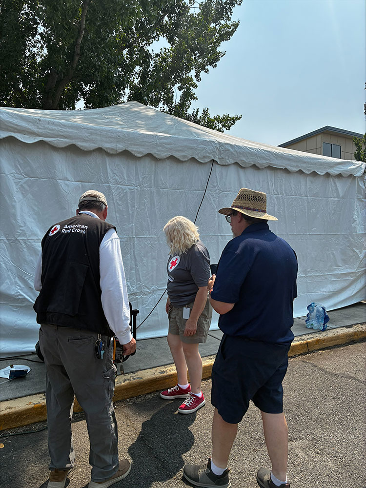 three Red Cross volunters next to the side of a shelter tent.