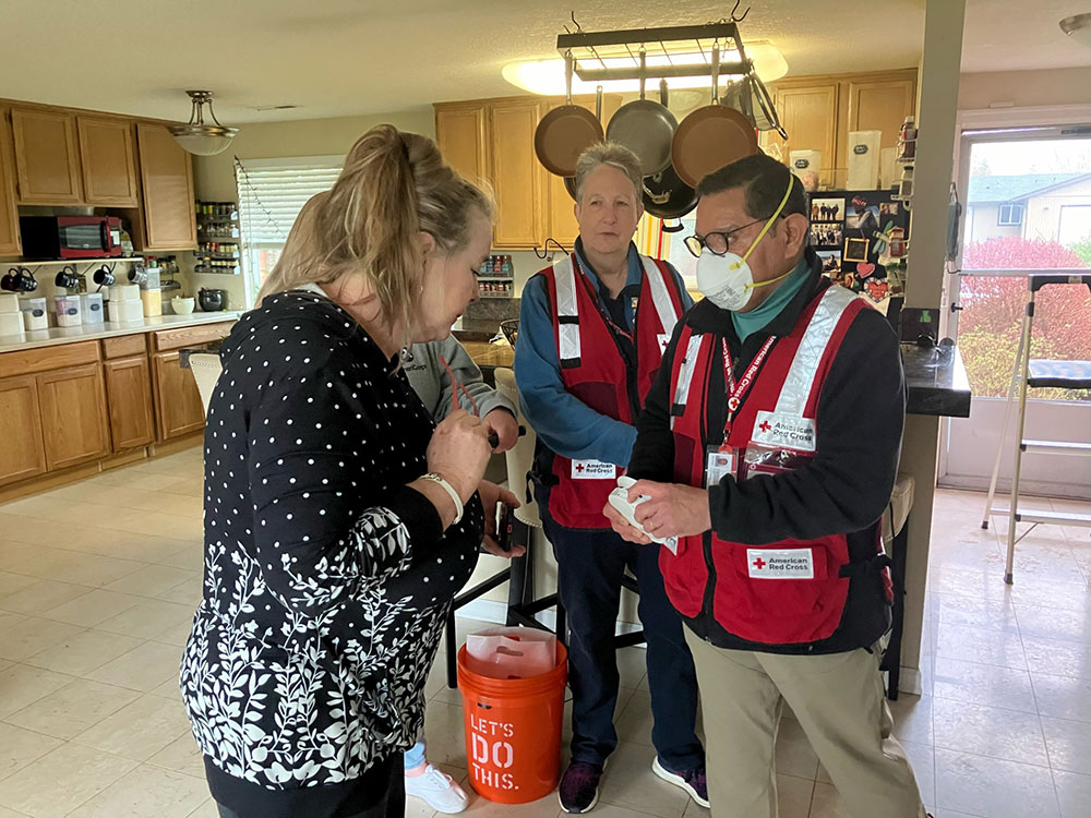 Red Cross volunteers showing a smoke alarm to a resident in their kitchen.