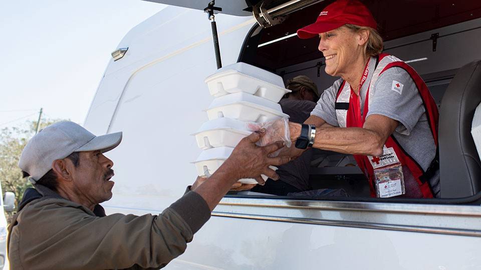 red cross volunteer susan williams serves warm meals to a resident from a red cross van.
