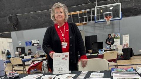 Jana Norton standing at a table with a Red Cross table cloth and pamphlets at a local Stand Down veteran’s event.