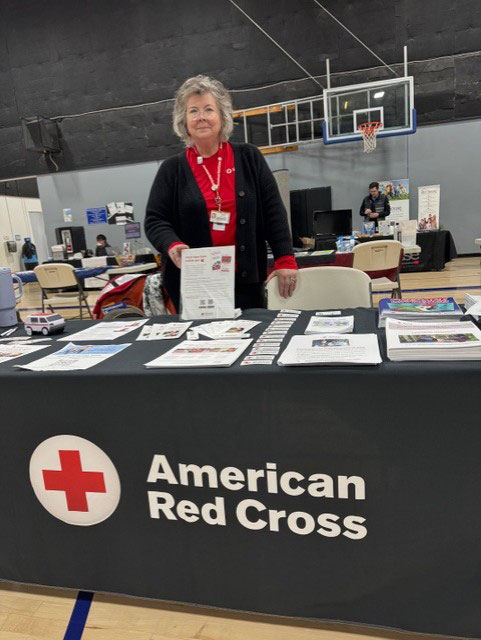 Jana Norton standing at a table with a Red Cross table cloth and pamphlets at a local Stand Down veteran’s event.