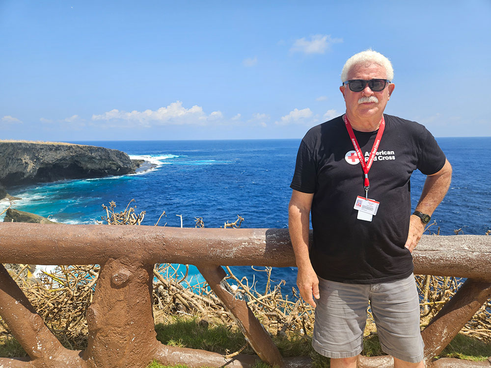  Jim Court stands on a wooden fence overlooking the ocean, with waves crashing in the background.