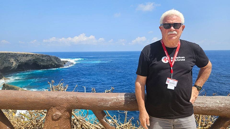  Jim Court stands on a wooden fence overlooking the ocean, with waves crashing in the background.