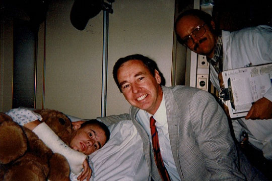 Kate Robinson in a hospital bed with a cast on her arm with her neurosurgeons standing next to her.