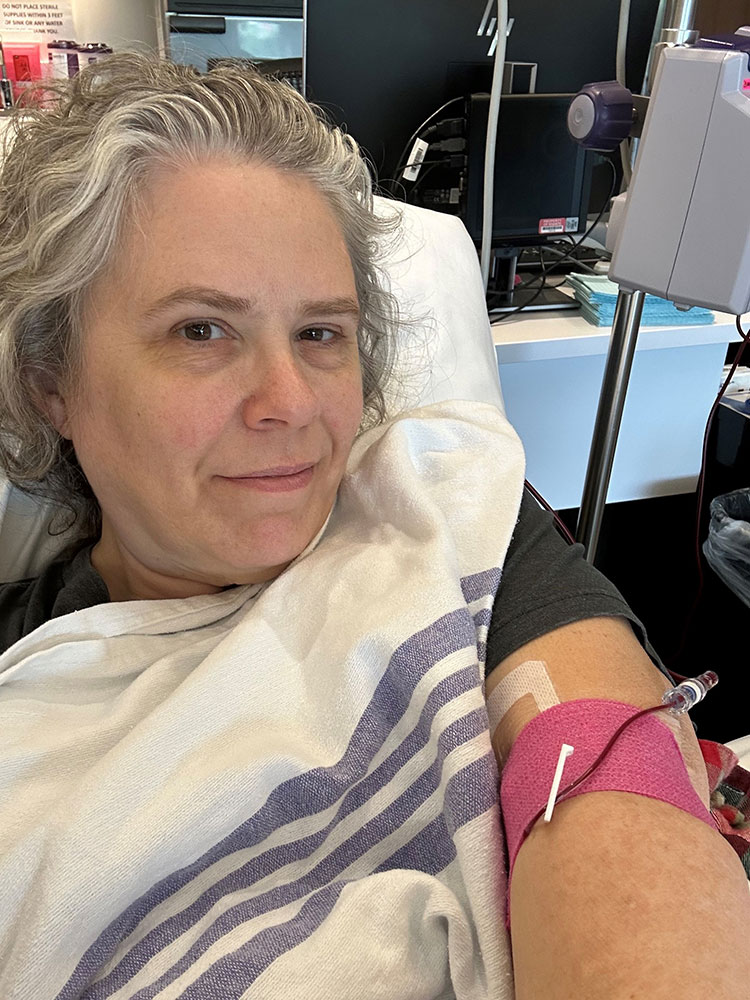 Katrina Long takes a selfie while in a hospital bed with a bandage and tube on arm.